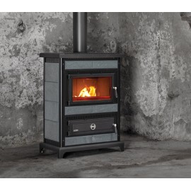 Un poêle à bois en métal noir avec une porte vitrée est installé contre un mur en béton texturé et brut. Le poêle est en marche, avec des flammes orange visibles à travers la porte vitrée. Un tuyau métallique s'étend verticalement depuis le haut du poêle.