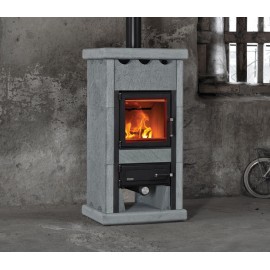 Un poêle à bois en pierre est présenté contre un mur en béton. Le poêle est doté d'une porte vitrée laissant apparaître un feu à l'intérieur. Il y a un tuyau d'aération au sommet et un compartiment sous le foyer. Le décor semble être un espace rustique ou inachevé.