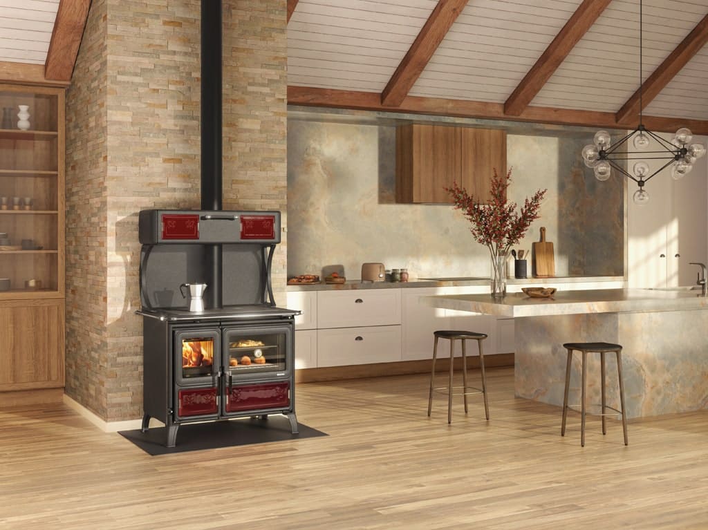 Une cuisine moderne avec parquet en bois dispose d'une cuisinière à bois de style vintage, d'un feu visible et d'une bouilloire sur le dessus. La cuisine est dotée d'un mur d'accent en pierre, d'armoires blanches, de tabourets de bar sur l'îlot et d'un lustre suspendu au plafond à poutres en bois.